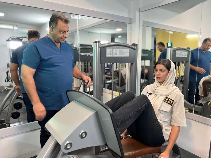 یکی از اعضای کادر کلینیک در حال تمرین با دستگاه پرس پا، زیر نظر دکتر امیرحسین شیربان